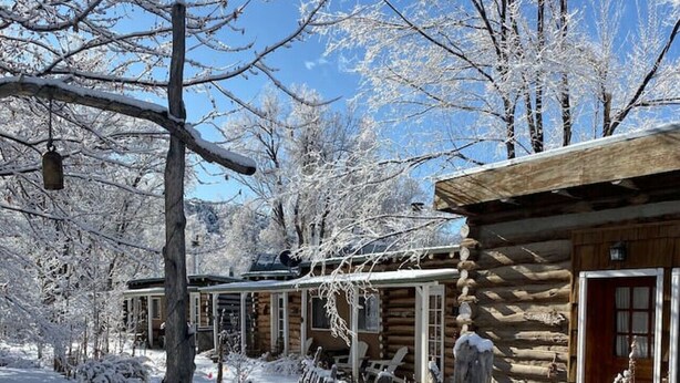 Une cabane en rondins avec un porche en bois, une pancarte indiquant la présence d’un jardin et des arbres couverts de neige.