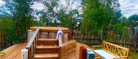 Una terraza de madera con un jacuzzi, escaleras de madera y un banco.