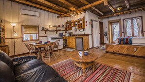 L’intérieur d’un chalet rustique comprend une table à manger en bois, un canapé, un coin cuisine et une grande fenêtre.