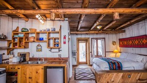 L’intérieur d’un chalet rustique, avec une cuisine en bois, un lit recouvert d’une couverture colorée et un plafond en bois.