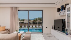 Un soggiorno moderno con vista piscina, un divano, una TV e un angolo bar.