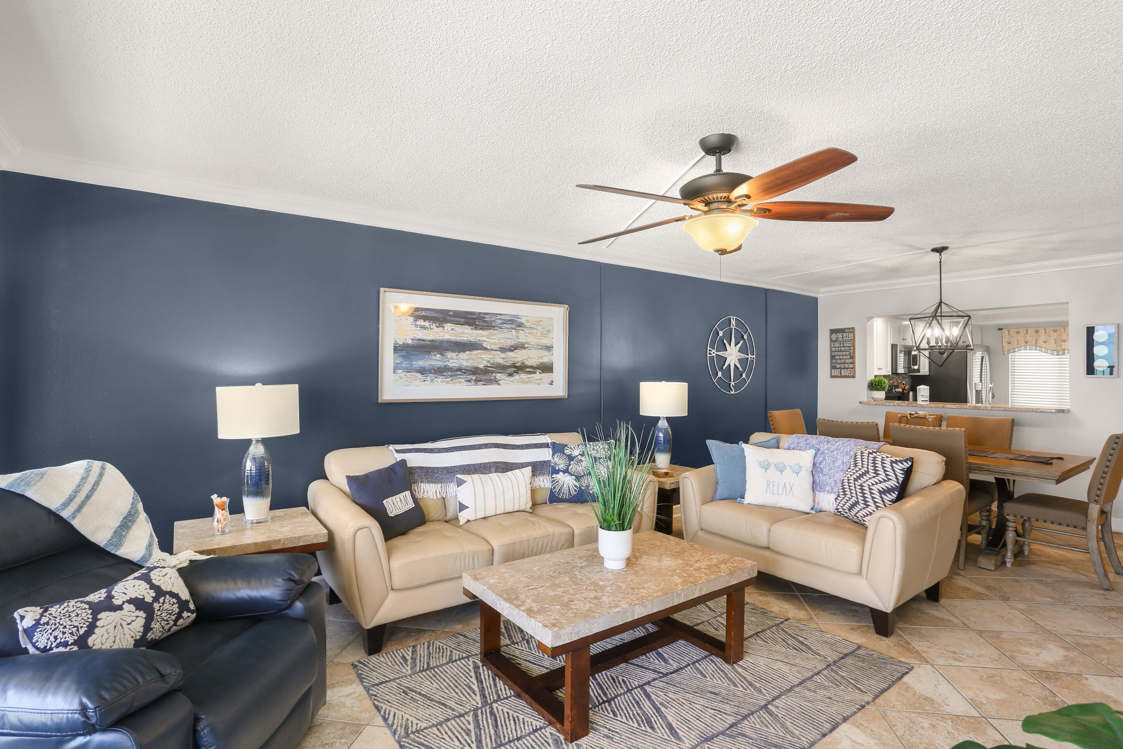 A living room with two sofas, a coffee table, a ceiling fan, and a dining area with a table and chairs.