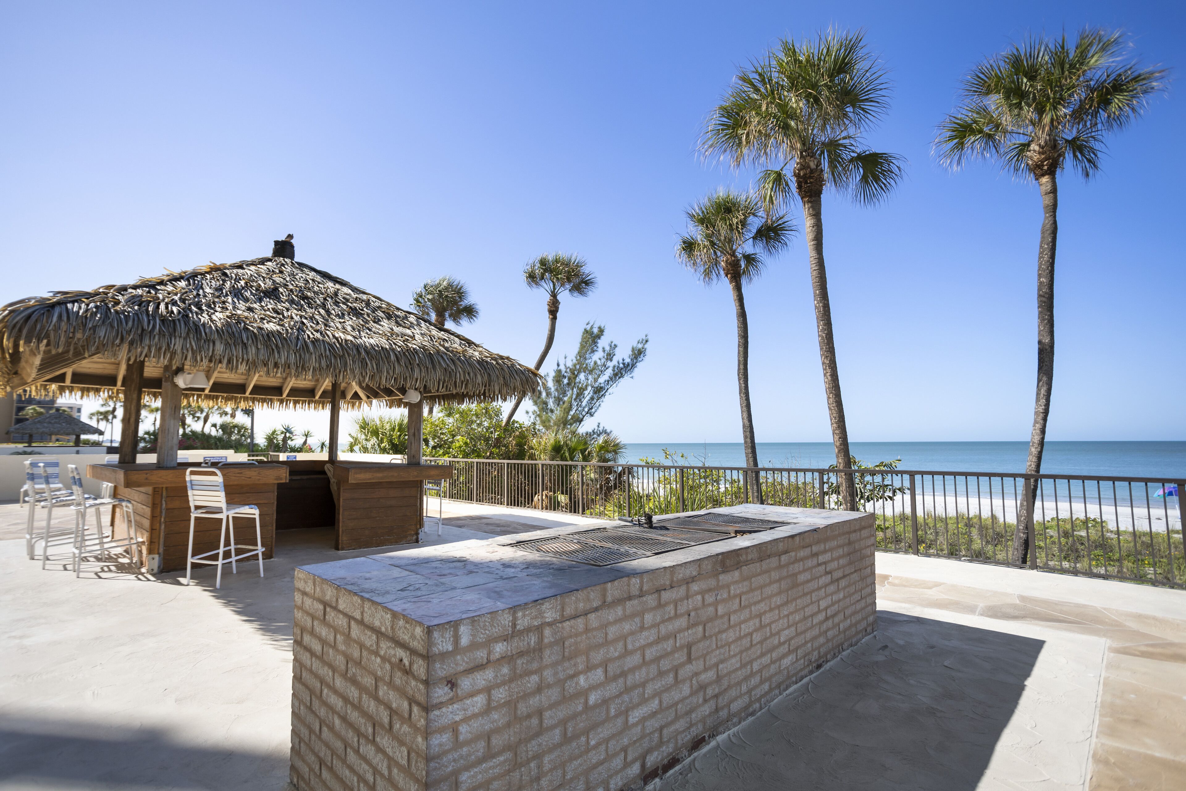 An outdoor bar area with a thatched roof, seating, and a view of the beach and ocean.