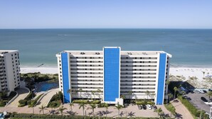 A hotel with a blue facade, a pool, and a beach view. - 🌅 Ocean Sands II #606 — Gulf Front Elegance with Sunset Views (Madeira Beach)