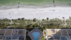 An aerial view of a beach resort with a swimming pool, beach area, and adjacent buildings. - 🌅 Ocean Sands II #606 — Gulf Front Elegance with Sunset Views (Madeira Beach)