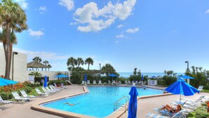 A pool area with lounge chairs and umbrellas, a clear sky, and a view of the ocean. - 🌅 Ocean Sands II #606 — Gulf Front Elegance with Sunset Views (Madeira Beach)