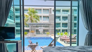 Ein Hotelzimmer mit einem großen Bett, einem Fernseher und Blick auf einen Swimmingpool sowie ein Gebäude mit Balkonen.