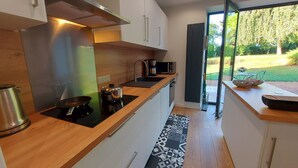 Una cocina moderna con encimera de madera, electrodomésticos de acero inoxidable y vista a un jardín por una puerta corredera.
