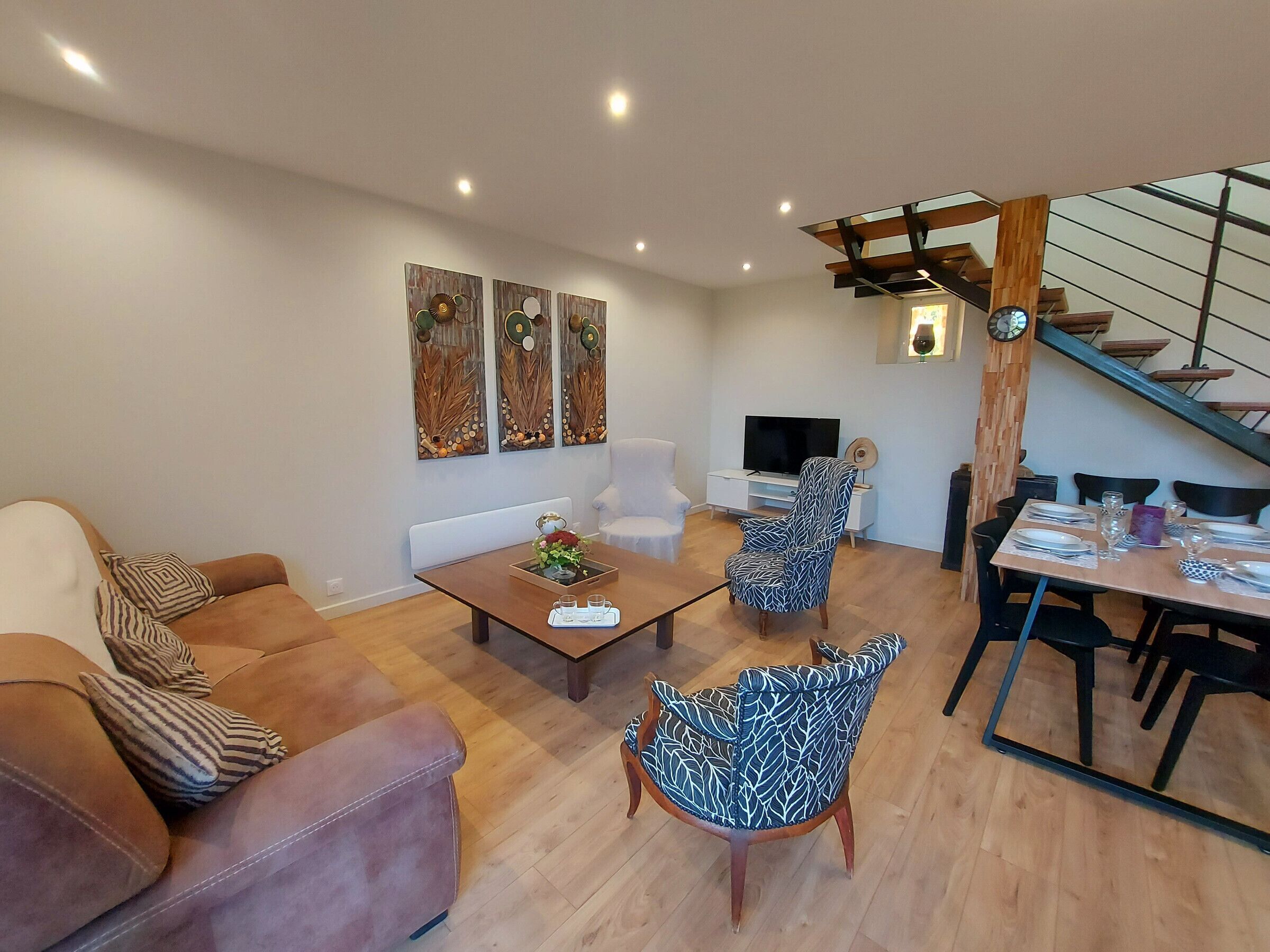 Ein modernes Wohnzimmer mit einer Couch, zwei gemusterten Sessel, einem Couchtisch und einem Essbereich mit Tisch für vier Personen.
