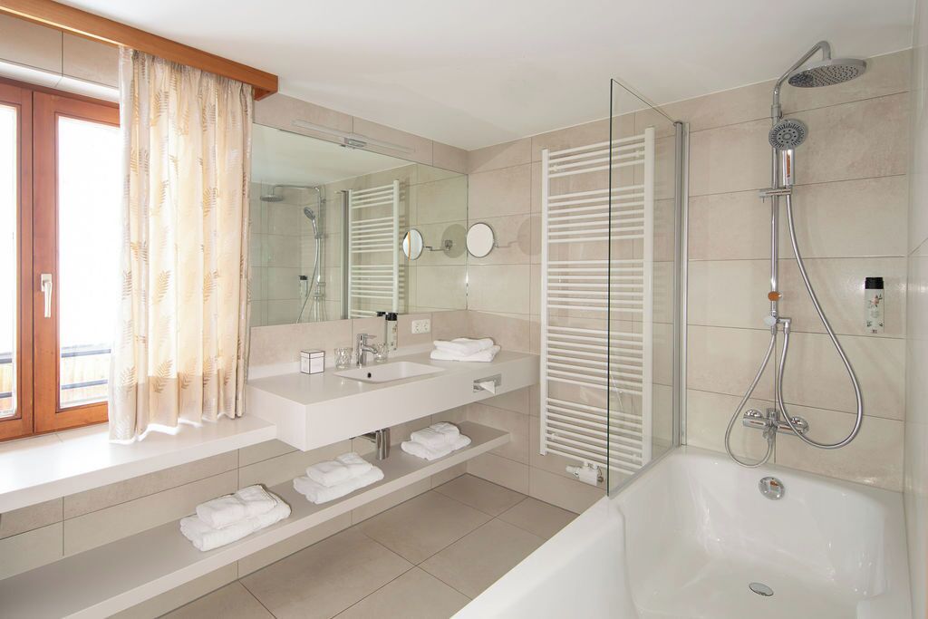 A modern bathroom with a large mirror, two sinks, a shower, and a bathtub.