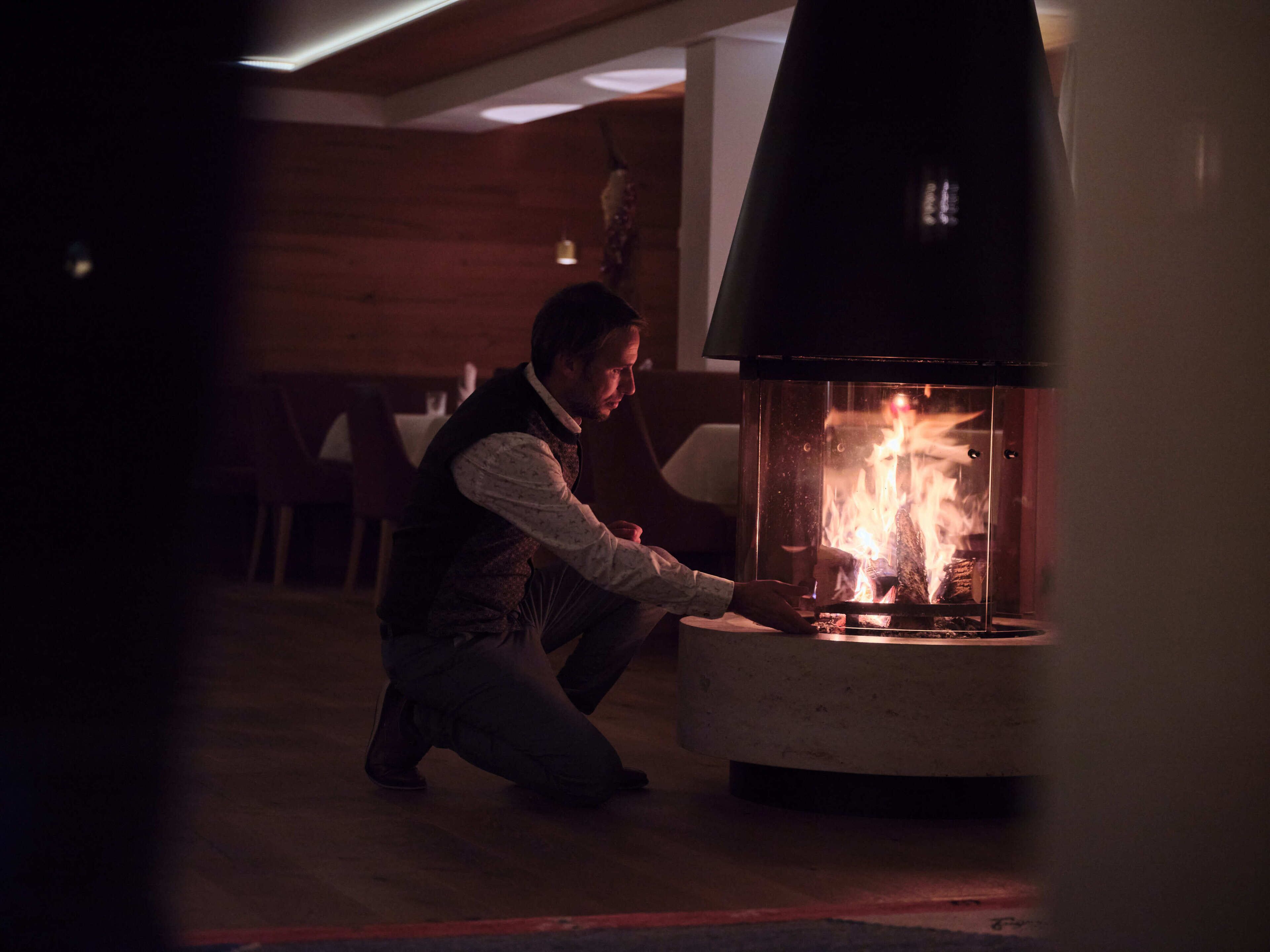 Una persona atendiendo un horno a leña en una habitación con paredes de madera y un banco al fondo.