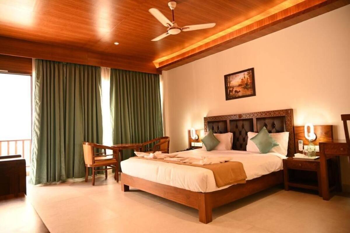 Quarto com teto de madeira, cama com almofadas, mesa de cabeceira, cadeira e um quadro na parede.