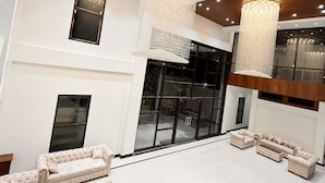 Un hall d’entrée spacieux, agrémenté de lustres modernes, de fauteuils confortables et de grandes fenêtres offrant une vue sur l’extérieur.
