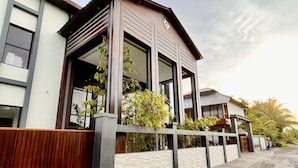 Une maison moderne à deux étages, dotée de grandes fenêtres, d’une clôture en bois et d’un mur en pierre.
