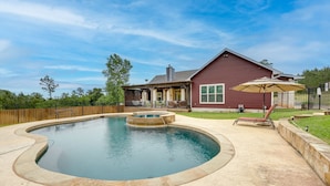A backyard with a swimming pool, a wooden deck, and a house with a red exterior. - Pool & Hot Tub in Sunny Smithville Getaway! (Smithville)