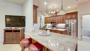 A kitchen with wooden cabinets, a granite countertop, stainless steel appliances, and a flat-screen TV. - Pool & Hot Tub in Sunny Smithville Getaway! (Smithville)