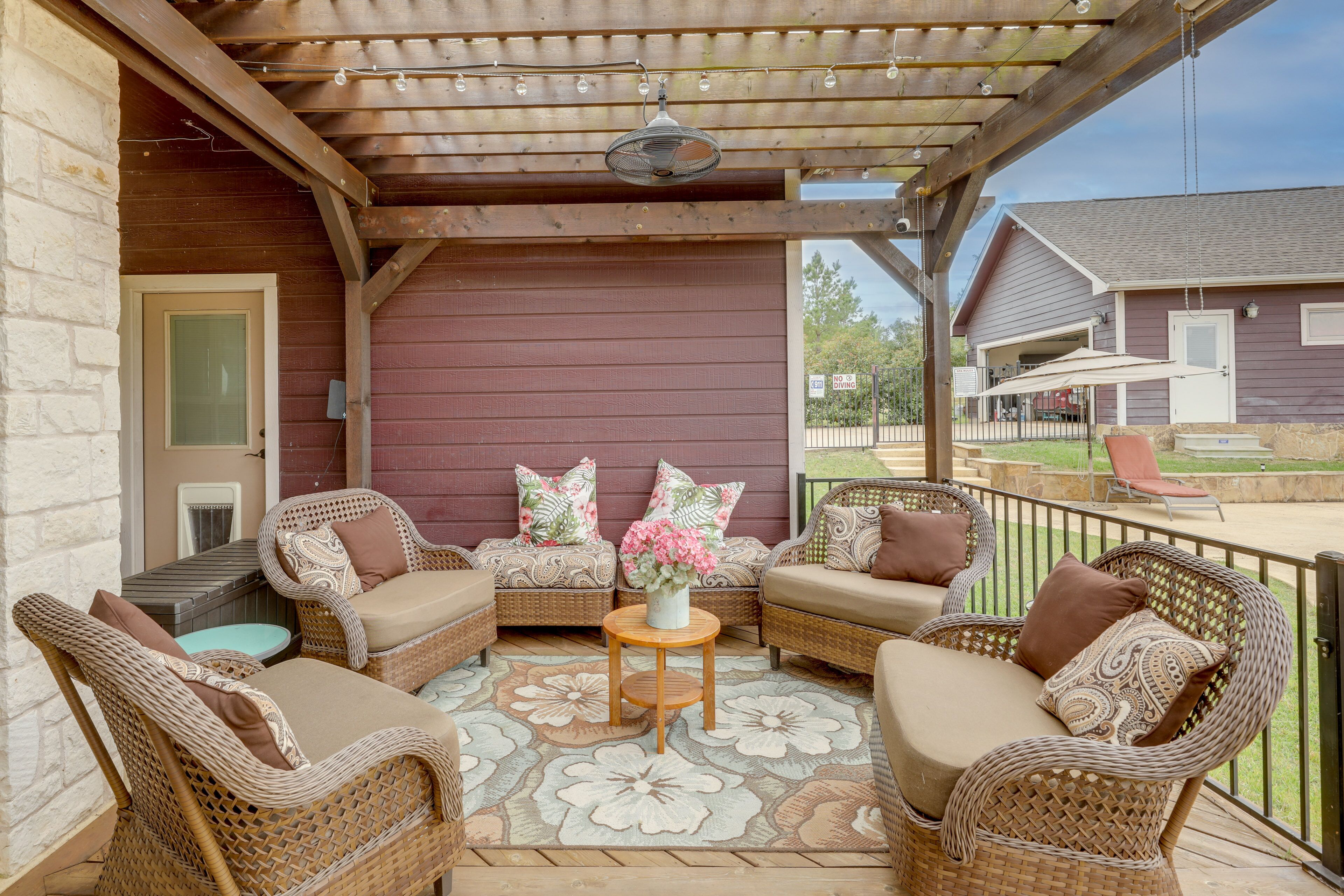 An outdoor patio with wicker furniture, a central table with a vase of flowers, and a covered area with a pergola.