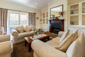 A living room with a fireplace, a sofa set, a coffee table, and a view through a large window.
