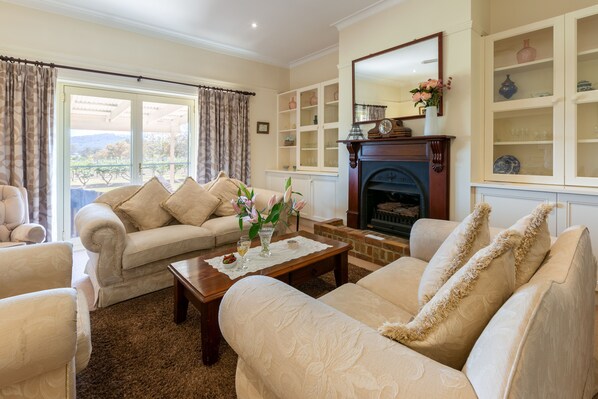 A living room with a fireplace, a sofa set, a coffee table, and a view through a large window.