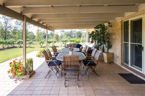 An outdoor patio with a round table and chairs, surrounded by potted plants and a view of a landscaped garden.
