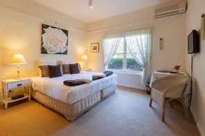 A hotel room with a large bed, bedside lamps, a TV, a window with curtains, and a wicker chair.