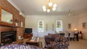 A living room with a fireplace, a television, a sofa set, and a dining area with chairs and a table. - Bluebush Estate - The Cottage (Rothbury)