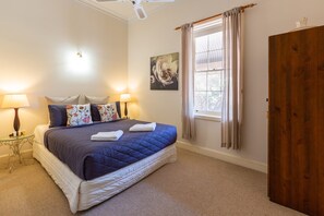 Een slaapkamer met een groot bed, twee nachtlampjes, een raam met gordijnen, een houten garderobe en een schilderij aan de muur.
