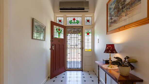 A hallway with a tiled floor, a wooden door with stained glass, a wall-mounted air conditioner, and a framed picture. - Bluebush Estate - The Cottage (Rothbury)