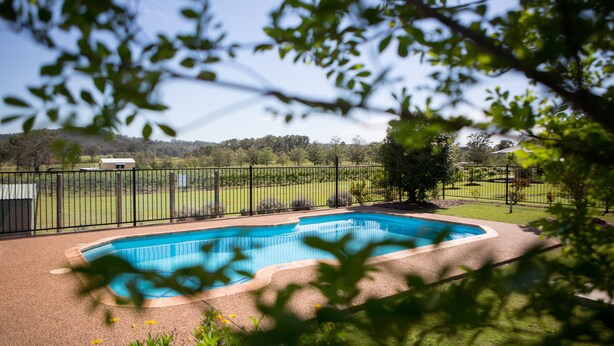 A swimming pool surrounded by a fenced area with a view of a green landscape and trees. - Bluebush Estate - The Chalet (Rothbury)