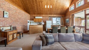 A cozy interior with a wooden ceiling, a dining area, and a seating area with a sofa. - Bluebush Estate - The Chalet (Rothbury)