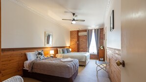 A hotel room with two beds, a sitting area with a chair, a ceiling fan, and a window with curtains. - Bluebush Estate - The Chalet (Rothbury)