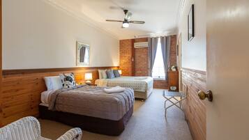 A hotel room with two beds, a sitting area with a chair, a ceiling fan, and a window with curtains.
