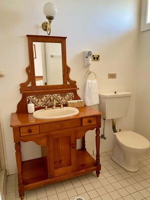 A bathroom with a wooden vanity, a mirror, a sink, a toilet, and a hairdryer on the wall. - Bluebush Estate - The Chalet (Rothbury)