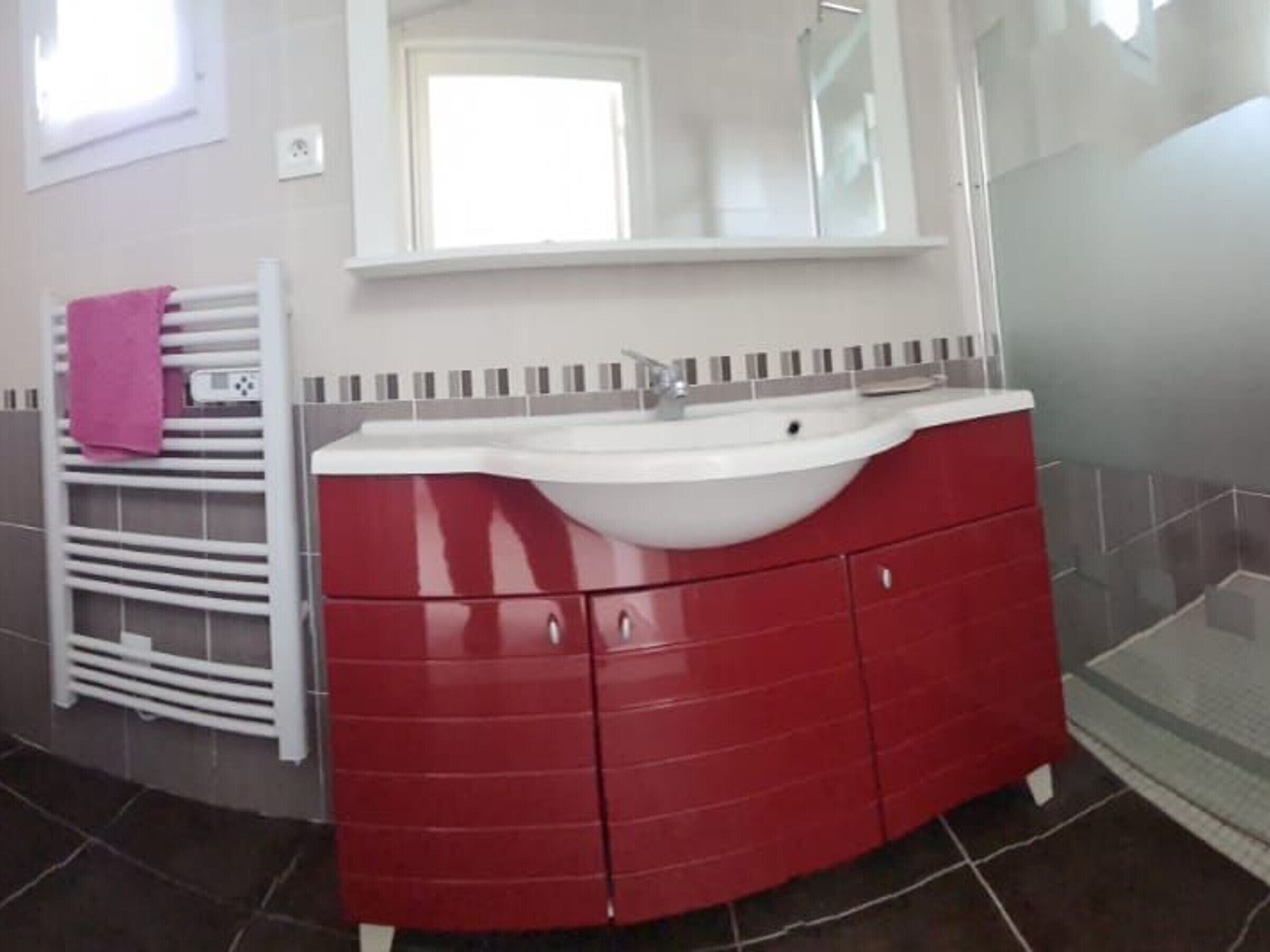 A bathroom with a red vanity, a white sink, and a mirror above it.