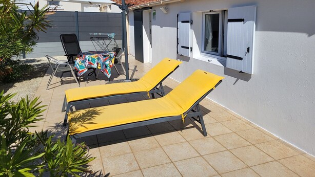 A patio with two yellow sun loungers, a table with a colorful tablecloth, and a white umbrella.