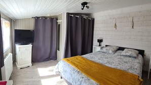 A bedroom with a bed, a TV, a nightstand, and a window with curtains.