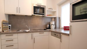 Uma cozinha moderna com armários brancos, uma pia de aço inoxidável, micro-ondas e cafeteira.