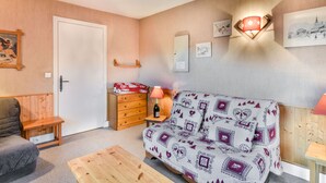 Ein gemütliches Zimmer mit Holzboden, einer Couch mit gemusterten Kissen, einem Holztisch, einem Schminktisch und einer Tür.