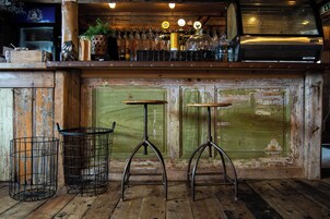 Un rústico espacio de bar con taburetes de madera, una puerta verde y una estantería con botellas y vasos.