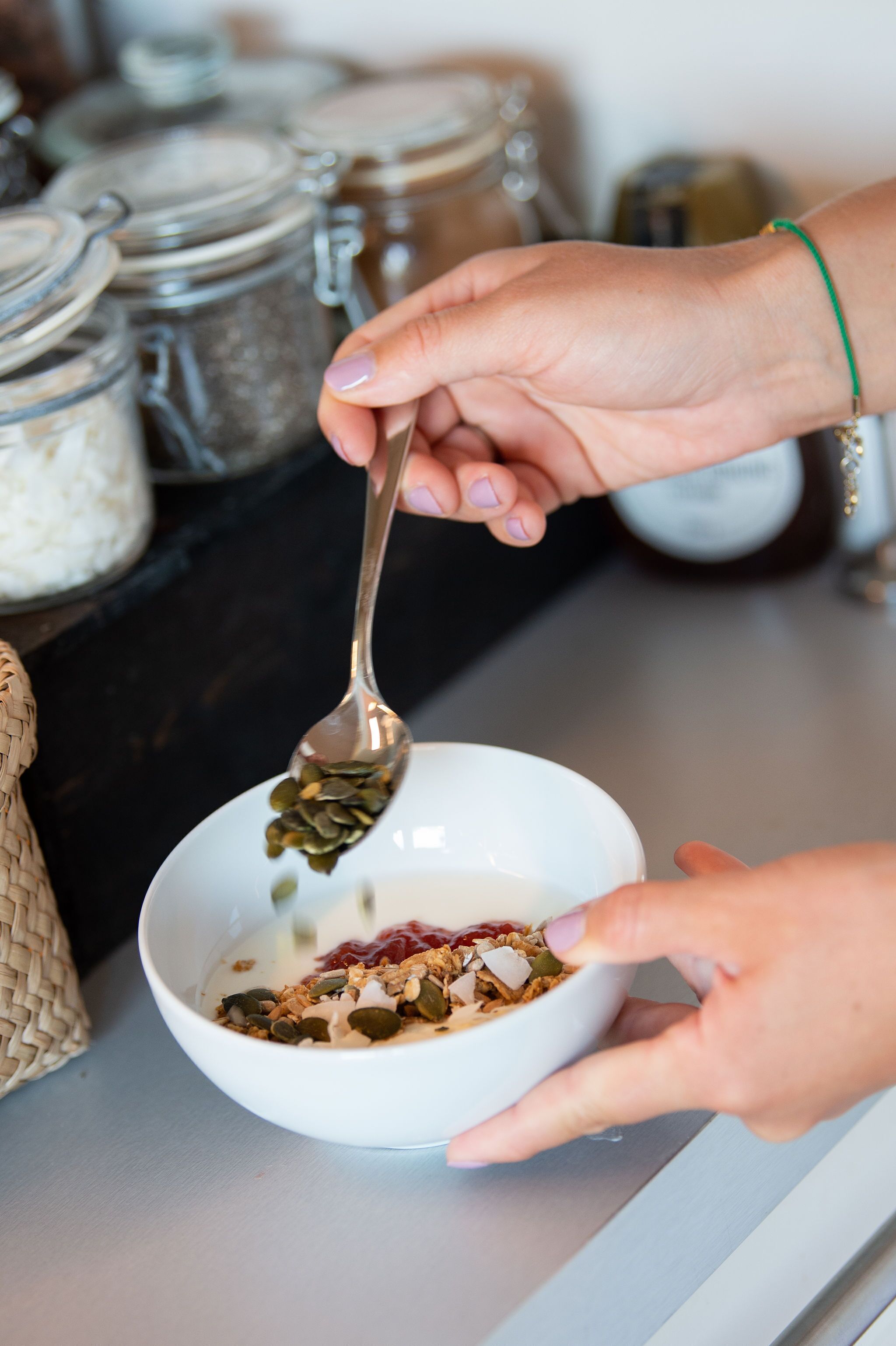 A person preparing a bowl of cereal with granola and seeds.