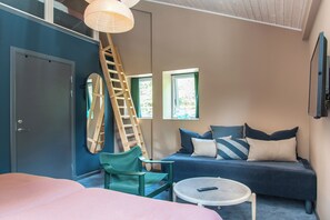 A room with a bed, a sofa, a small round table, a chair, a ladder, and a window.