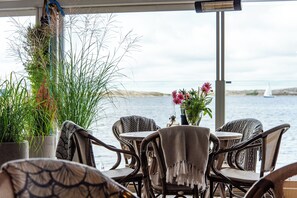 A seaside restaurant with wicker chairs and tables, potted plants, and a view of the sea. - Grundéns Hotell (Grundsund)