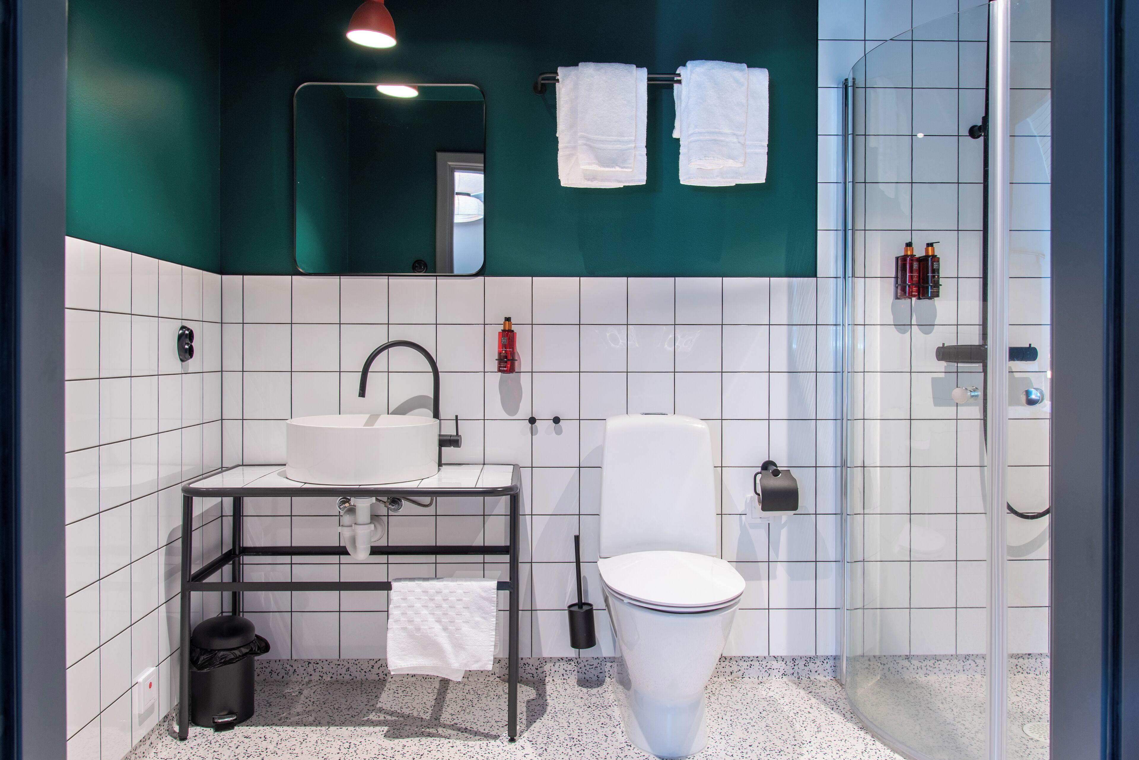A modern bathroom with a white sink, toilet, and shower. There are two towels hanging on a rack, and a mirror above the sink.