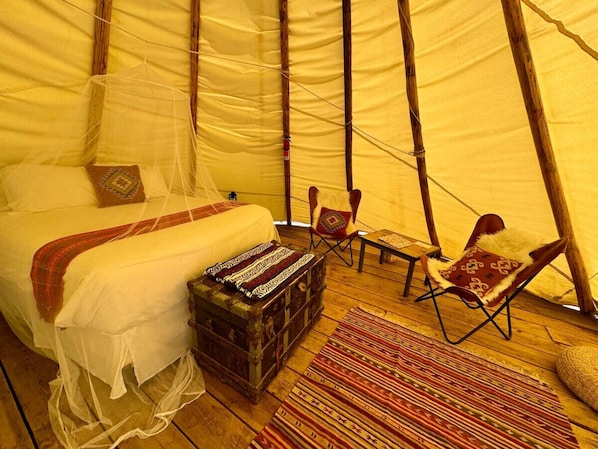 A tent with a bed, two chairs, a small table, and a woven basket.