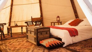 A tent with a bed, a table, a chair, a chest, and a lantern.