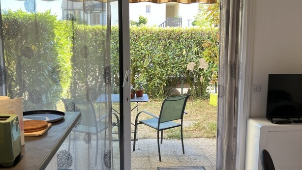 A room with a sliding glass door leading to an outdoor area with a chair and a table. - Central 1BR Garden Apartment, Close to Beach, Parking & Pet-Friendly (Cabourg)
