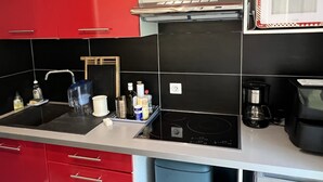 A modern kitchen with red cabinets, a black countertop, and a built-in stove. - Central 1BR Garden Apartment, Close to Beach, Parking & Pet-Friendly (Cabourg)