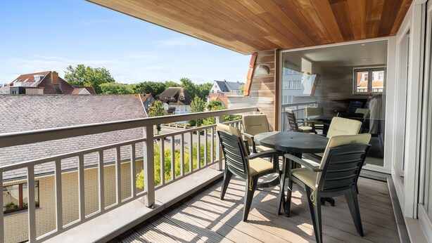 Ein Balkon mit Holzboden, einem Tisch mit Stühlen und Blick auf angrenzende Häuser.