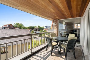A balcony with a wooden ceiling, a table with chairs, and a view of neighboring houses.