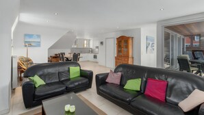 Ein modernes Wohnzimmer mit zwei schwarzen Ledersofas, einem Glastisch und einem Essbereich im Hintergrund.